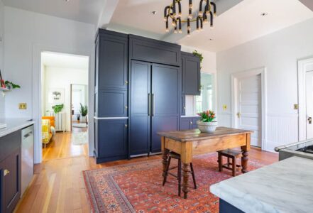 Standing island in the middle of a vintage kitchen with two stools on opposite ends next to a built-in refrigerator.
