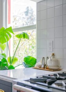 A wooden platter with salt and pepper grinders and a small vase next to a kitchen window.
