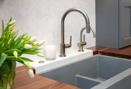Elevated stone base kitchen sink nested under a wooden countertop with a stainless steel faucet.