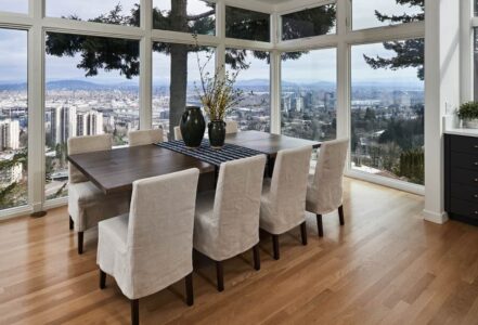 Long wooden kitchen table with eight high-back chairs with grey seat covers.