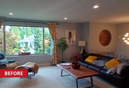 Carpeted living room with a black couch with orang pillows, an oak wood coffee table, and an eames lounge chair and ottoman.