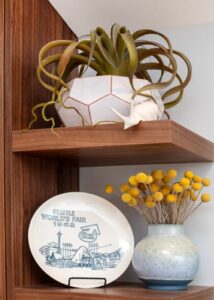 Stacked medium-dark wood grain floating shelves with a plant on top and plate displayed next to a vase of flowers below.