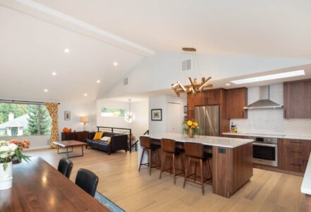 Kitchen with medium-dark wood grain cabinetry, white dimensional backsplash tile, a kitchen island with a waterfall countertop, and matte black fixtures.