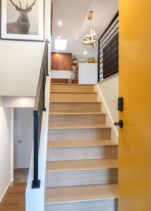 Stairs with a matte black high-visibility stair railing gong up to a kitchen.