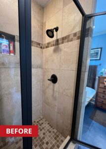 Shower with a swinging door and black shower knobs and shower head.