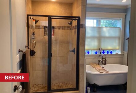 Shower with a swinging door and black shower knobs and shower head.