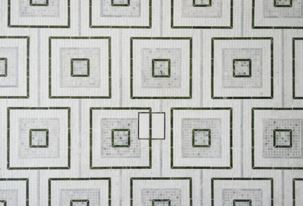 Toilet in a transitional bathroom with green tile and mosaic marble floor.