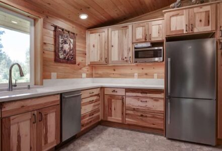 Fully renovated cabin kitchen with stainless steel appliances, a white countertop, and finished wooden cabinets.
