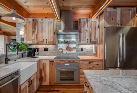 Fully renovated cabin kitchen with stainless steel appliances, a white countertop, and finished wooden cabinets.