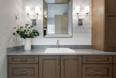 Bathroom white sink below a haning mirror with two light sconces on each side.