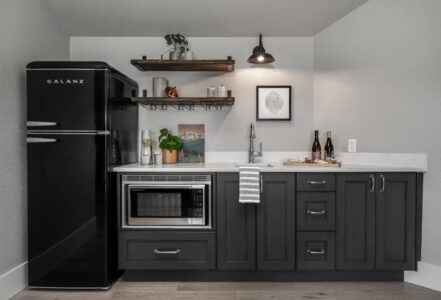 Kitchen space with a black refrigerator to the left of a kitchen wet bar.