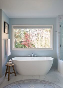 Signature Hardware oval acrylic freestanding tub below a window.