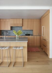 A modern kitchen featuring warm wooden cabinetry, a sleek island with bar stools, and a touch of greenery on the countertop.