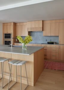 A modern kitchen featuring warm wooden cabinetry, a sleek island with bar stools, and a touch of greenery on the countertop.