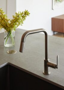 A modern kitchen faucet with a sleek design, positioned beside a vase of yellow flowers on a stone countertop, creating a stylish and functional space.