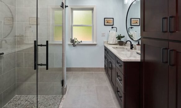 A modern bathroom with a glass shower, dark wood vanity, and light blue walls.