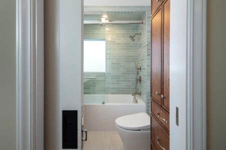 A remodeled bathroom with wood cabinets and green shower tile