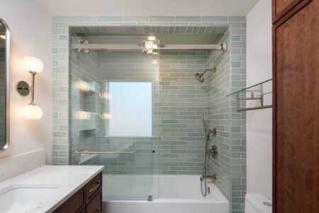 A remodeled bathroom with wood cabinets and soft green shower tile